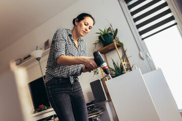 Woman in casual clothing sitting on the floor of her apartment and assembling furniture