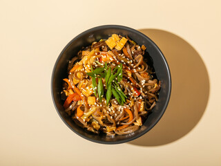 Top view of noodles in a black bowl isolated on beige background.