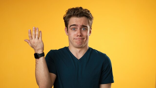 Portrait of happy young man 20s shrugging shoulders and gesturing I do not know isolated on yellow background.