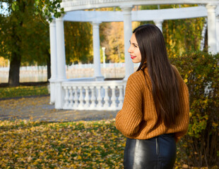 Autumn lifestyle, a young Caucasian brunette, in a black skirt and with a seductive look, in a park by a lake.