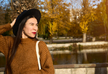 Close-up portrait of girl in a black hat and brown coat eye winks at the camera and smiles while holding white bag.Sun shining in the corner. Selective focus and copy space.