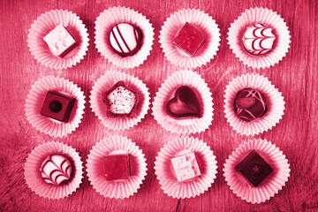 Viva Magenta color of the year 2023. Top view on assorted chocolate pralines on wooden surface
