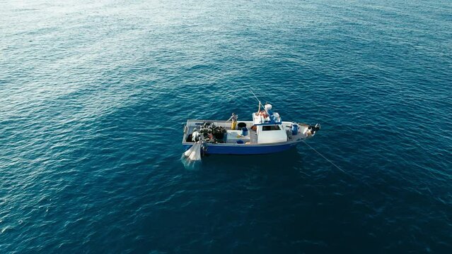 Lonely trawler in deep blue sea with fishers working together to pull out their catch of fresh ocean fish
