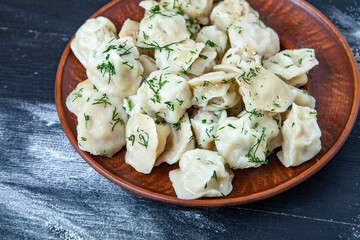 Traditional russian pelmeni or ravioli, dumplings with meat on wood black background. Russian food and russian kitchen concept.