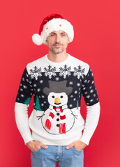 Handsome man in a winter sweater and Santa hat on studio red background.