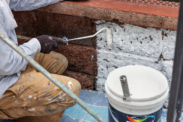 Painter worker adding undercoat foundation paint onto wall with roller at residential building in...