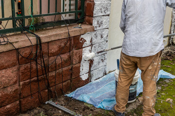 Painter worker adding undercoat foundation paint onto wall with roller at residential building in...