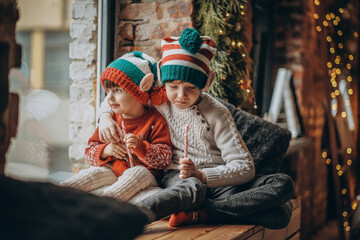 Fototapeta na wymiar Two little brother boys are sitting near the window and waiting for Christmas and Santa Claus. Happy childhood and Christmas.