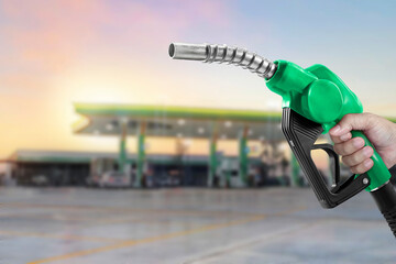 Holding a fuel nozzle against with gas station blurred background - obrazy, fototapety, plakaty