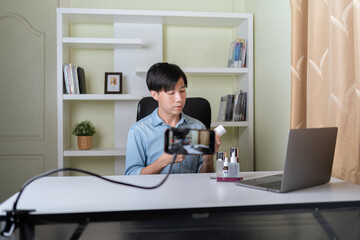 Young adult Asian beauty video blogger man filming, online live streaming his video blog about male cosmetic, male skincare. Guy looking camera to show new skin care for men product, teaching make up.