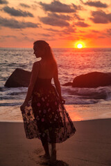 View back silhouette woman standing on sandy beach at sea sunset background, looking away. Rear...