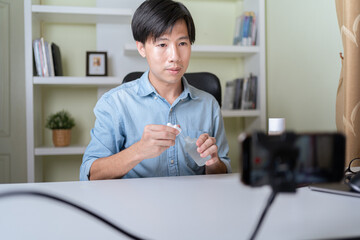 Young adult Asian beauty video blogger man filming, online live streaming his video blog about male cosmetic, male skincare. Guy looking camera to show new skin care for men product, teaching make up.