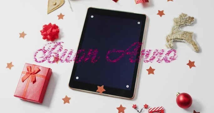 Animation of buen anno text over christmas decorations and tablet