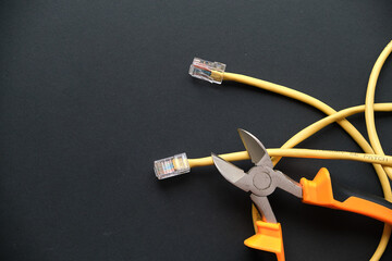 pliers and yellow internet cable on a black background. the concept of turning off wired internet...