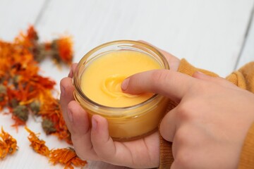 Small boy using calendula ointment. Medicinal cream from dried marigold flowers good for skin. White wooden table. - obrazy, fototapety, plakaty