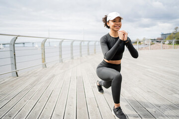 A woman does an active fitness workout on the street in sportswear and sneakers - obrazy, fototapety, plakaty