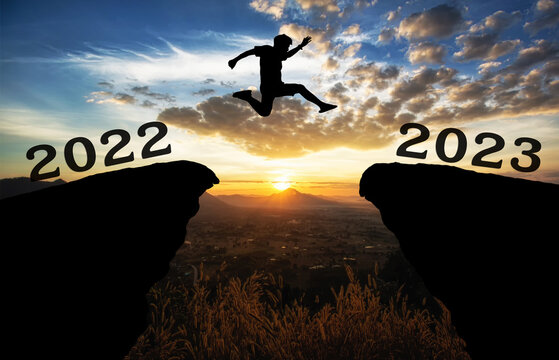 A young man jump between 2022 and 2023 years over the sun and through on the gap of hill silhouette evening colorful sky. happy new year 2023.	