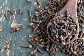 Dried cloves in a wooden spoon and scattered over a rustic wood table. Overhead top view of spices.