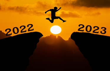A young man jump between 2022 and 2023 years over the sun and through on the gap of hill silhouette...