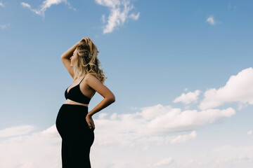 Pregnant woman wearing all black standing against blue cloudy sky. 