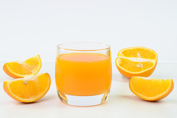 Orange juice in a glass cup and orange slices in the background.