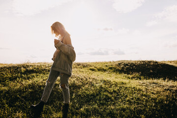Blonde pregnant woman wearing a denim jacket, moving in an open field.