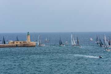 Sailing boats passing the lighthouse on the Valletta Breakwater at the entrance to the Grand Harbour, Valletta, Malta.