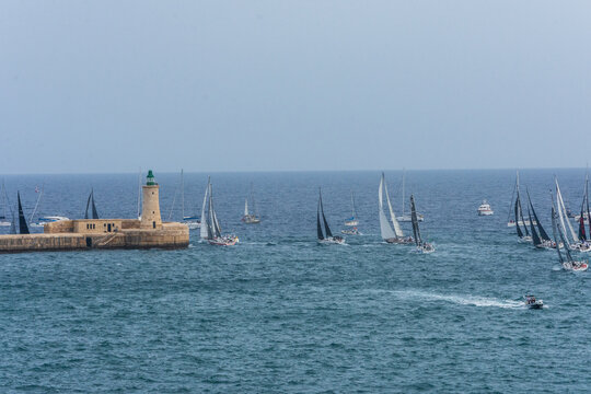 Sailing boats passing the lighthouse on the Valletta Breakwater at the entrance to the Grand Harbour, Valletta, Malta.