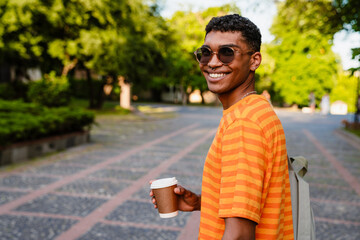 Fototapeta premium Young african man with backpack drinking coffee while standing outdoors