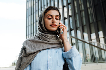 Young muslim woman talking on cellphone while standing outdoors