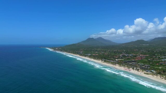 Aerial panoramic view of the Playa El Agua tropical beach on the Margarita island, Venezuela. Turquoise water of the Caribbean big waves, clear blue sky and mountains.