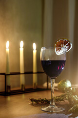 A glass of wine in front of lit candles with a low depth of sharpness. Christmas atmosphere.