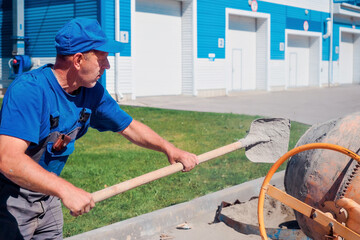 Uniformed construction worker works on construction site on summer day. Elderly bricklayer shovels...