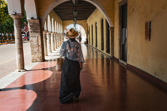 Young woman back view wearing hat walking throung the arch corridor in the historical part of Valladolid town, Mexico