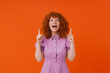 Excited redhead girl pointing fingers up at copy space isolated