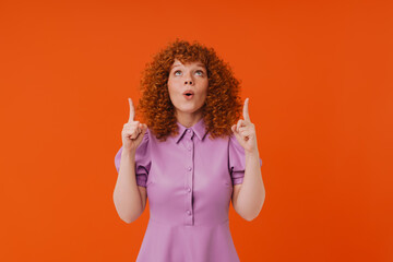 Excited redhead girl pointing fingers up at copy space isolated