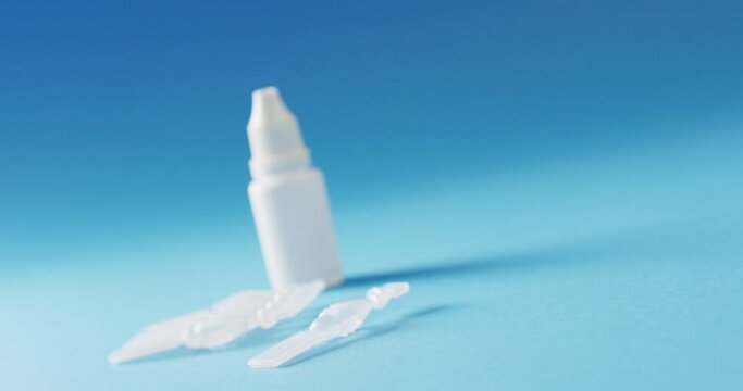 Rack focus video of saline caplets and dropper bottle on blue background with copy space