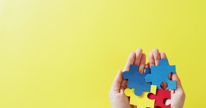 Video of hands holding jigsaw puzzle pieces on yellow background with copy space