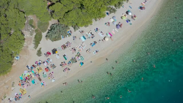 Secluded nudist beach in the blue lagoon near the city of Makarska Croatia. Vacationers frolic in the warm Adriatic Sea. Summer vacation, sunbathing, fresh air. Drone view. Nugal Beach. Relax