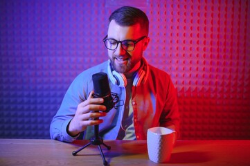 Young man recording or streaming podcast using microphone at his small broadcast studio. Content creator.