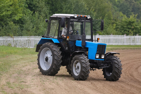 A blue tractor is driving a village road