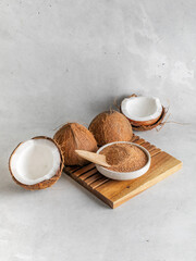 Natural bio brown coconut  sugar in a bowl on wooden stand closeup with coconut  on stone background