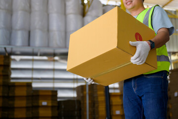 Asian male worker lifting cardboard boxes Inside a retail warehouse filled with shelves full of...
