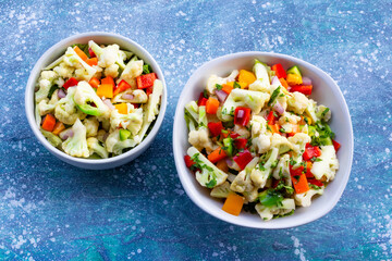 Healthy cauliflower salad in white bowl on blue wood background.