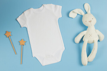 White cotton baby short sleeve bodysuit with soft plush sleeptoy bunny and natural wooden toy on light blue background. Infant onesie mockup. Gender neutral newborn bodysuit template mock up. Top view