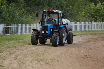 Tractor rides on the road and sprinkles the dust with water before horse races