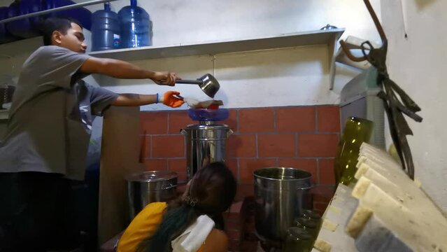 Asian woman manually bottling fruit wine, the man pouring fermented juice into stainless dispenser as they work in a small home local winery