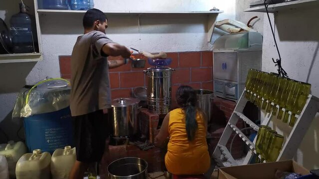 Asian woman manually bottling fruit wine, the man pouring fermented juice into stainless dispenser as they work in a small home local winery