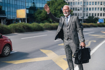 Elderly professional with laptop bag waving for taxi cab in the city.