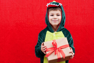 Portrait of beautiful child with box in his hands, decorated with red ribbon, isolated on red background. boy dressed in carnival costume holds gift in his hands. Happy New Year and Merry Christmas